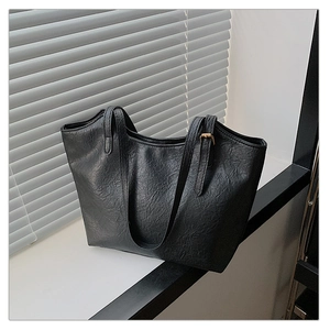 Close-up of black tote bag showing wrinkled faux leather texture and gold buckle