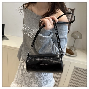 Détail d'un sac cylindrique noir brillant avec chaîne en argent et texte mode
