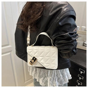 Detailed back view of white quilted crossbody bag with gold lock on a leather jacket