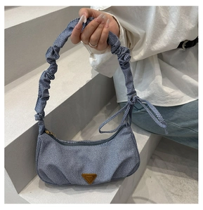 Dettaglio della borsa a mezzaluna in denim azzurro con tracolla a ruche e logo d'oro