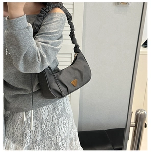 Detailed view of dark grey hobo bag with pleated strap and triangular metal plaque