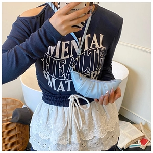 Detail of light blue pleated croissant bag worn by a model in a cozy indoor setting