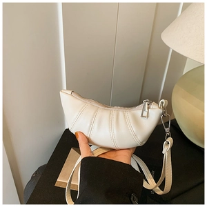 Detail of a creamy white pleated croissant bag with silver zipper and slim strap