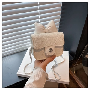 Detail of white quilted mini bag featuring silver camellia clasp and oversized bow decoration