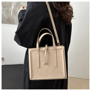 Detail view of a beige minimalist square crossbody bag with knot pendant and gold hardware