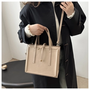 Close-up of a beige rectangular crossbody bag with dual handles and a slim shoulder strap