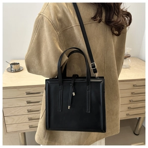 Detail of a minimalist black leather tote bag featuring gold hardware and drawstring tassels