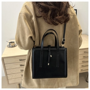 Detail of minimalist black leather handbag with gold metal hardware and long shoulder strap