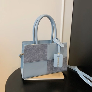 Light blue patchwork handbag with top handles and shoulder strap on a black table