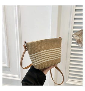 Detail of hand-woven straw crossbody bag with striped texture and brown leather strap