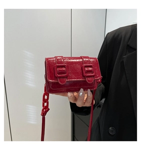 Detail of red patent leather mini bag with glossy wrinkled texture and dual square buckles