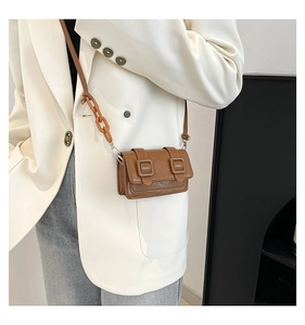 Close-up of a brown mini crossbody bag with resin chain strap on a white blazer outfit