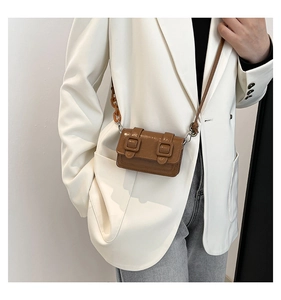Detail of brown glossy crossbody bag with amber acrylic chain and buckle straps