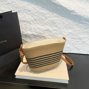 Striped straw bucket bag with brown leather strap displayed on books against a stone wall