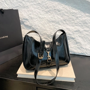Glossy black leather crescent saddle bag with gold clasp on minimalist book display