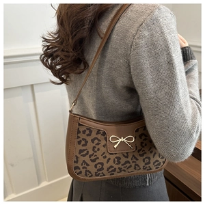 Detail view of leopard print shoulder bag with gold bow clasp on a minimalist model