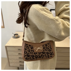 Detail of leopard print underarm bag featuring a gold bow buckle and brown leather trim