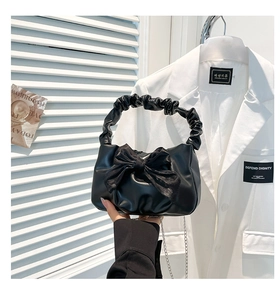 Close-up of black pleated handbag featuring a large bow and elegant metal chain strap