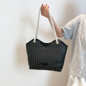 Detail of black woven straw tote bag with thick white rope handles and metal eyelets