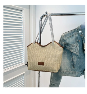 Detail of woven straw tote bag featuring brown leather trim and cotton rope handles