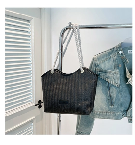 Detail of woven black tote bag featuring thick white cotton rope handles and fashion label