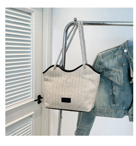 Detail of woven tote bag with rope handles and leather patch on herringbone fabric