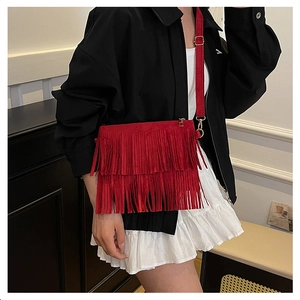 Detail of red tassel crossbody bag shown on model with adjustable strap and metal hardware