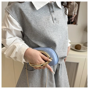 Detail of light blue glossy pillow bag with large gold U-shaped handle and chain