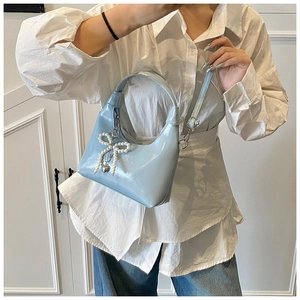 Detail of light blue glossy handbag featuring a pearl bow and metal heart charm