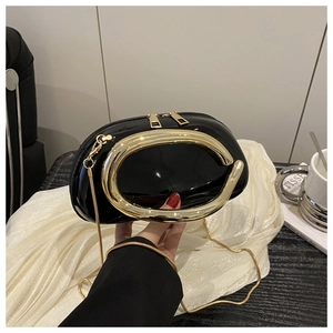 Detail of glossy black patent leather bag with gold C-shaped handle and snake chain