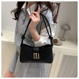 Model wearing a black leather shoulder bag with a gold buckle in a modern interior