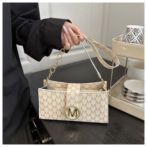 Detail of beige shoulder bag featuring M-pattern print and gold metallic M-clasp closure
