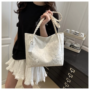 Detail of white lace embroidery on a large tote bag with woven rope handles and tassel
