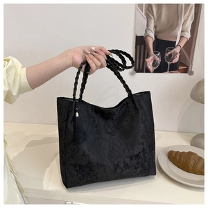 Close-up of black lace tote bag featuring elegant floral jacquard patterns and tassel detail
