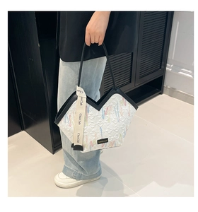 Detail of white quilted tote bag with black trim and elegant fashion letter ribbon charm