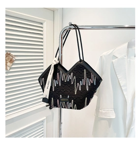 Close-up of black tote bag featuring colorful zigzag embroidery and metal fashion tag