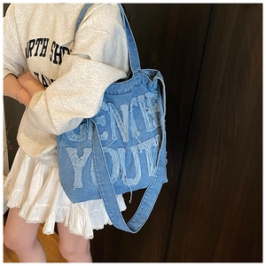 Detail of blue denim tote bag featuring vintage frayed letter patchwork and fabric texture