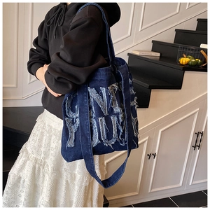 Detail of blue denim tote bag featuring frayed edge embroidery and wide shoulder straps