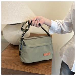 Détail d'un sac bandoulière en nylon vert armée avec fermetures éclair et étiquette cuir