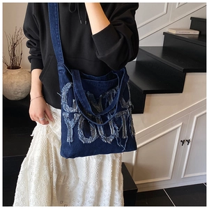 Detail of distressed denim tote bag featuring frayed letter patches and sturdy handle