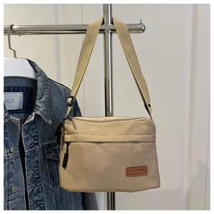 Détail de la sacoche en nylon beige avec bandoulière réglable et étiquette en cuir