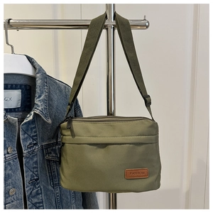 Détail du sac bandoulière en nylon vert olive avec étiquette en cuir sur veste en jean