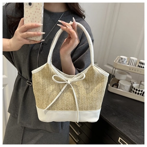 Close-up of natural straw shoulder bag with white leather bow detail and sturdy handles