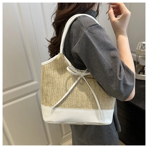 Detail of a straw woven tote bag with a white leather bow and textured shoulder strap