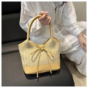 Detail of straw woven tote with yellow leather trim and bowknot on a white shirt