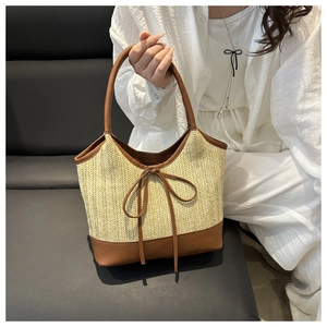 Detailed close-up of straw tote bag with brown leather trim and decorative bow detail