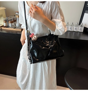 Detail of a black glossy PU shoulder bag featuring a cute white alpaca plush charm
