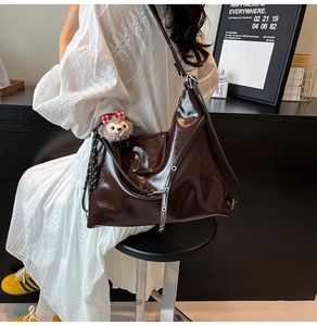 Detail of dark brown glossy patent leather shoulder bag with plush bear charm accessory
