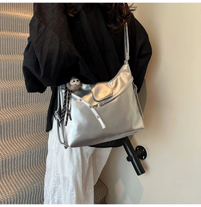 Detailed side view of silver glossy tote bag with plush animal charm on a shoulder
