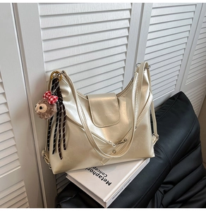 Detail of metallic champagne tote bag with a cute plush bear charm on a white book